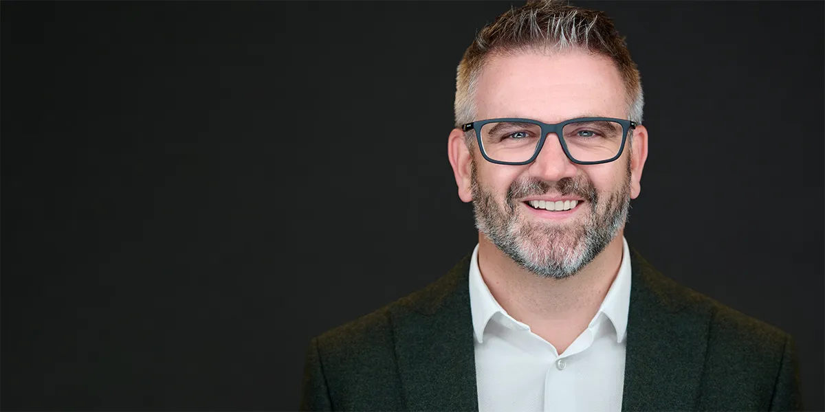 Confident professional man with glasses smiling against a dark background — Bristol headshot photographer.