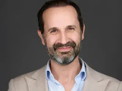 Corporate headshot of executive with beard wearing light grey blazer and blue shirt, demonstrating approachable leadership style for professional team photography