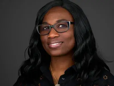 Corporate headshot of professional woman with glasses and long dark hair wearing black blazer, demonstrating inclusive and professional corporate team photography