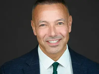 Corporate headshot of executive with close-cropped hair wearing navy suit and green tie, showcasing confident professional leadership for corporate team photography