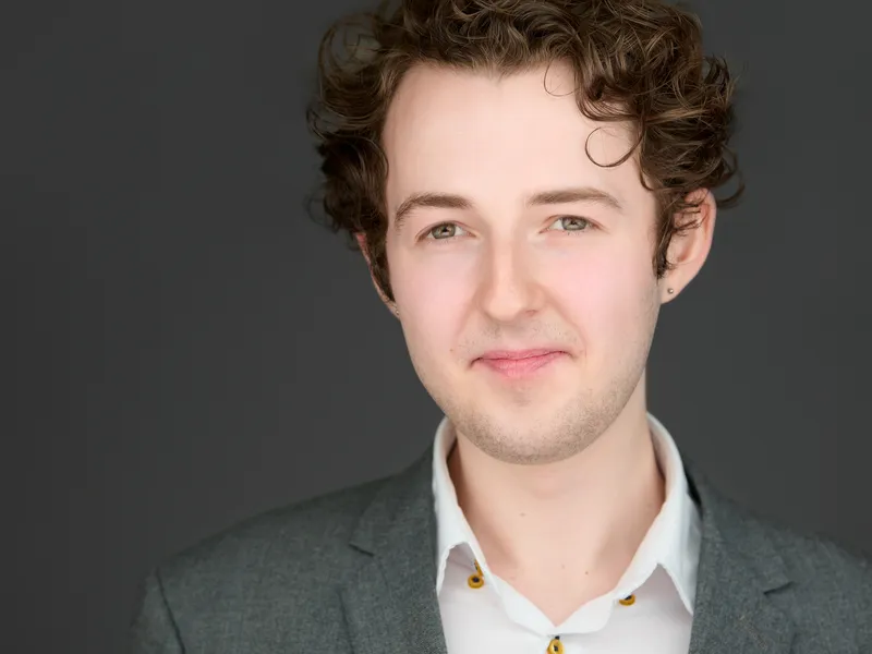 Young professional man with curly hair in grey blazer and white shirt with unique collar details, fresh approachable look