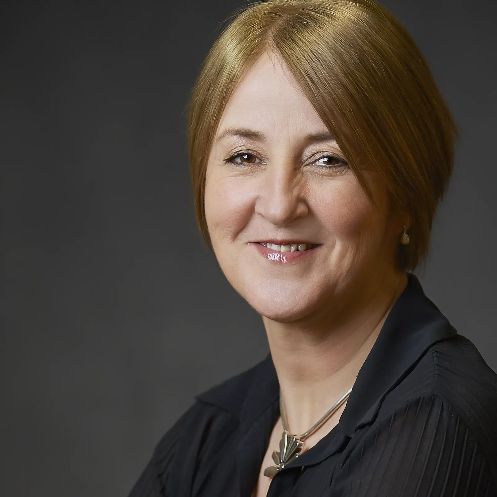 Professional business headshot of an older woman with a grey background captured