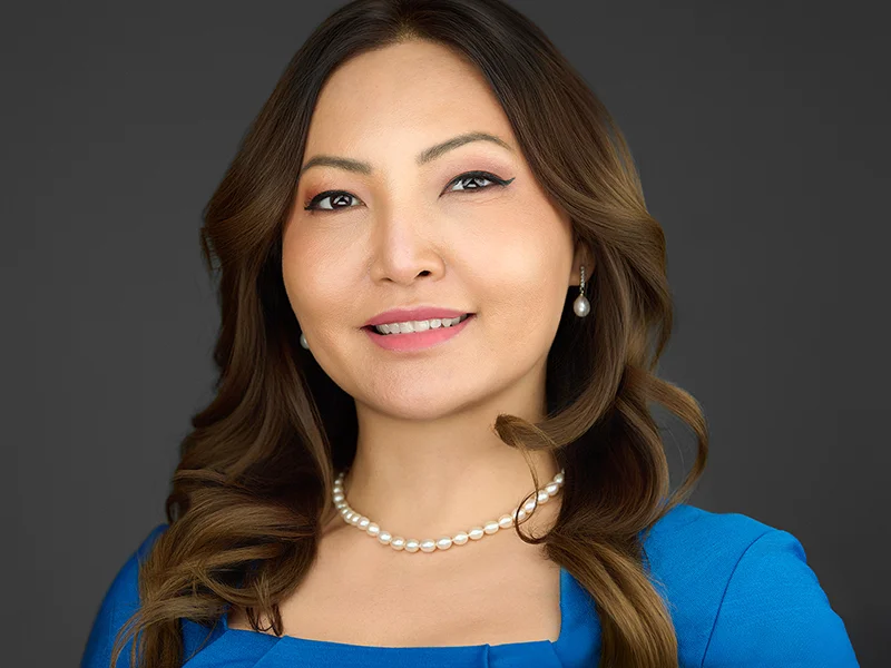 Business headshot of an Exeter woman in blue jacket smiling against dark background