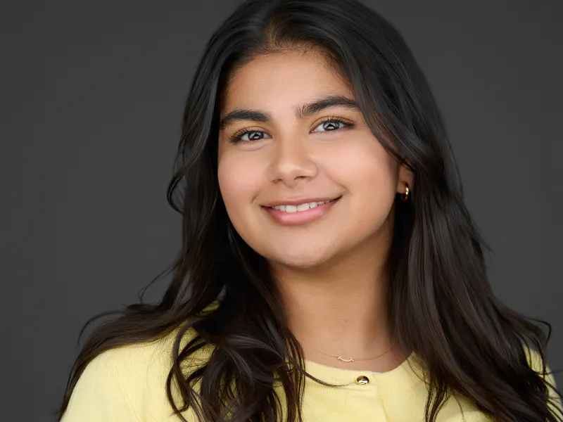 Falmouth Professional Photography | Young Women's Business Headshots Young professional woman with long dark hair in yellow top and delicate necklace, bright smile