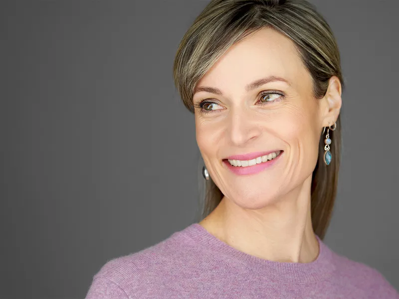 Falmouth Business Photography | Executive Women's Professional Portraits Executive woman in purple sweater with statement earrings, sophisticated side-glancing smile