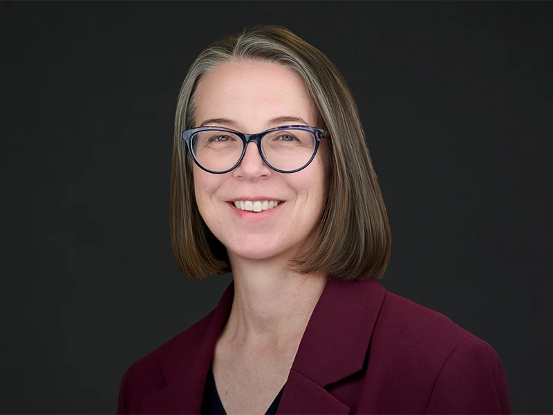 Smiling woman in burgundy blazer and glasses, modern corporate portrait on dark background