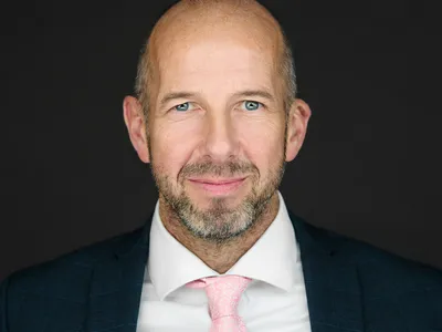 Bald executive in dark suit with pink tie, confident professional business headshot