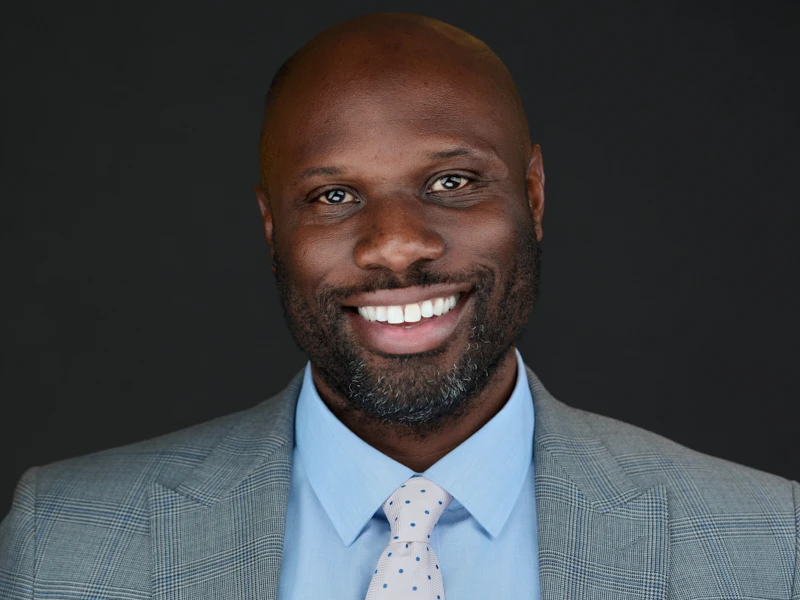Executive headshot of a smiling man in a light grey suit and blue shirt, photographed by ProHeadshots UK.