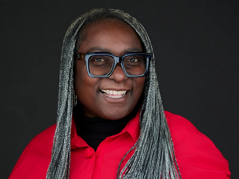 Professional headshot of a confident woman wearing glasses and a red blouse against a dark background, photographed by ProHeadshots UK.