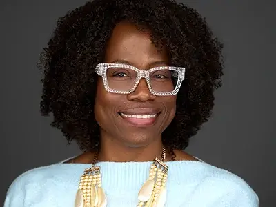 Confident professional with statement glasses, light blue top, layered necklace, natural curls, modern business portrait