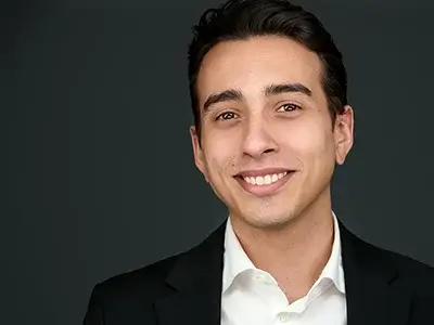 Professional male portrait with dark background, business attire, warm smile, contemporary corporate headshot style