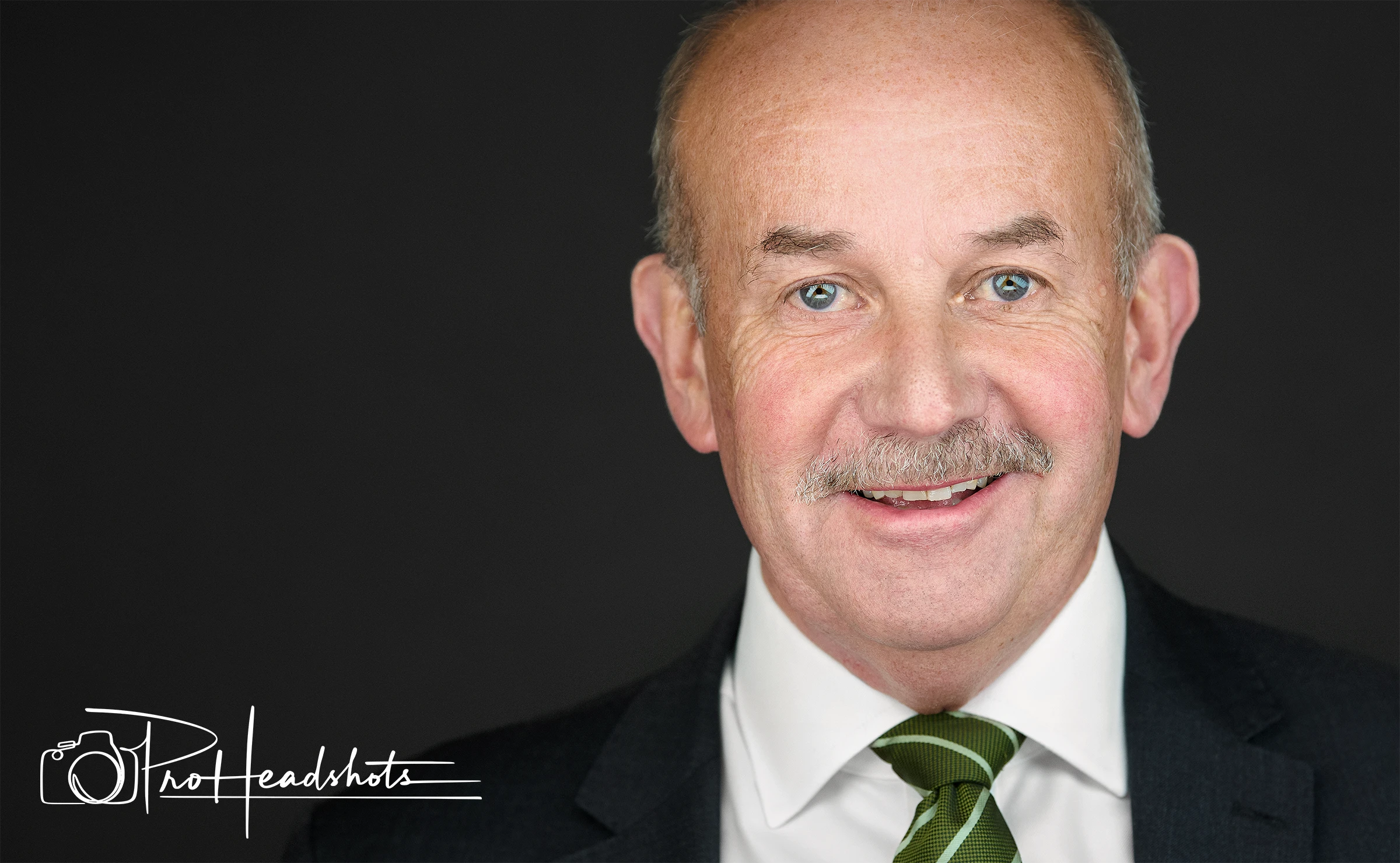 Image of an older businessman wearing a suit and a green neck tie