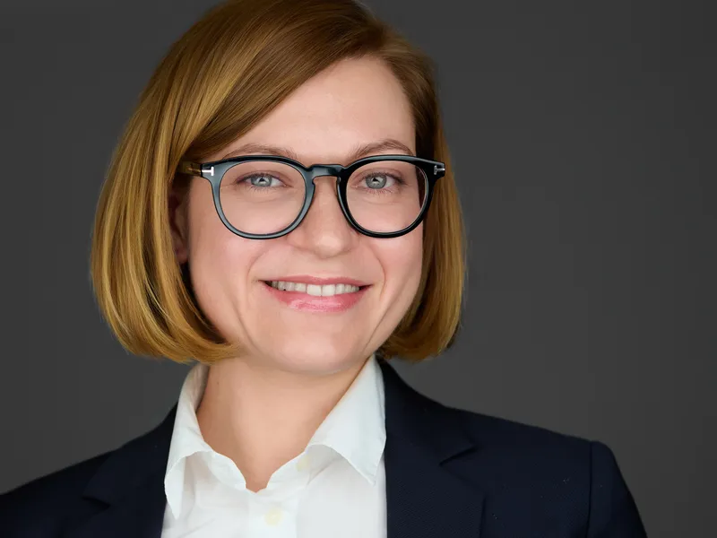Professional woman in navy blazer and white shirt with round glasses, approachable business headshot