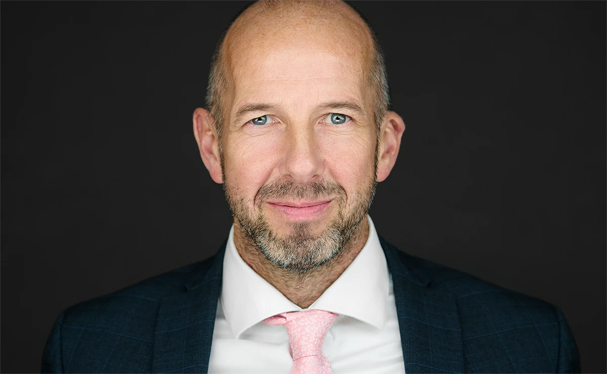 The Confidence Connection: How the Right Photographer Brings Out Your Best Professional headshot of man with beard in navy suit and pink tie against dark background.