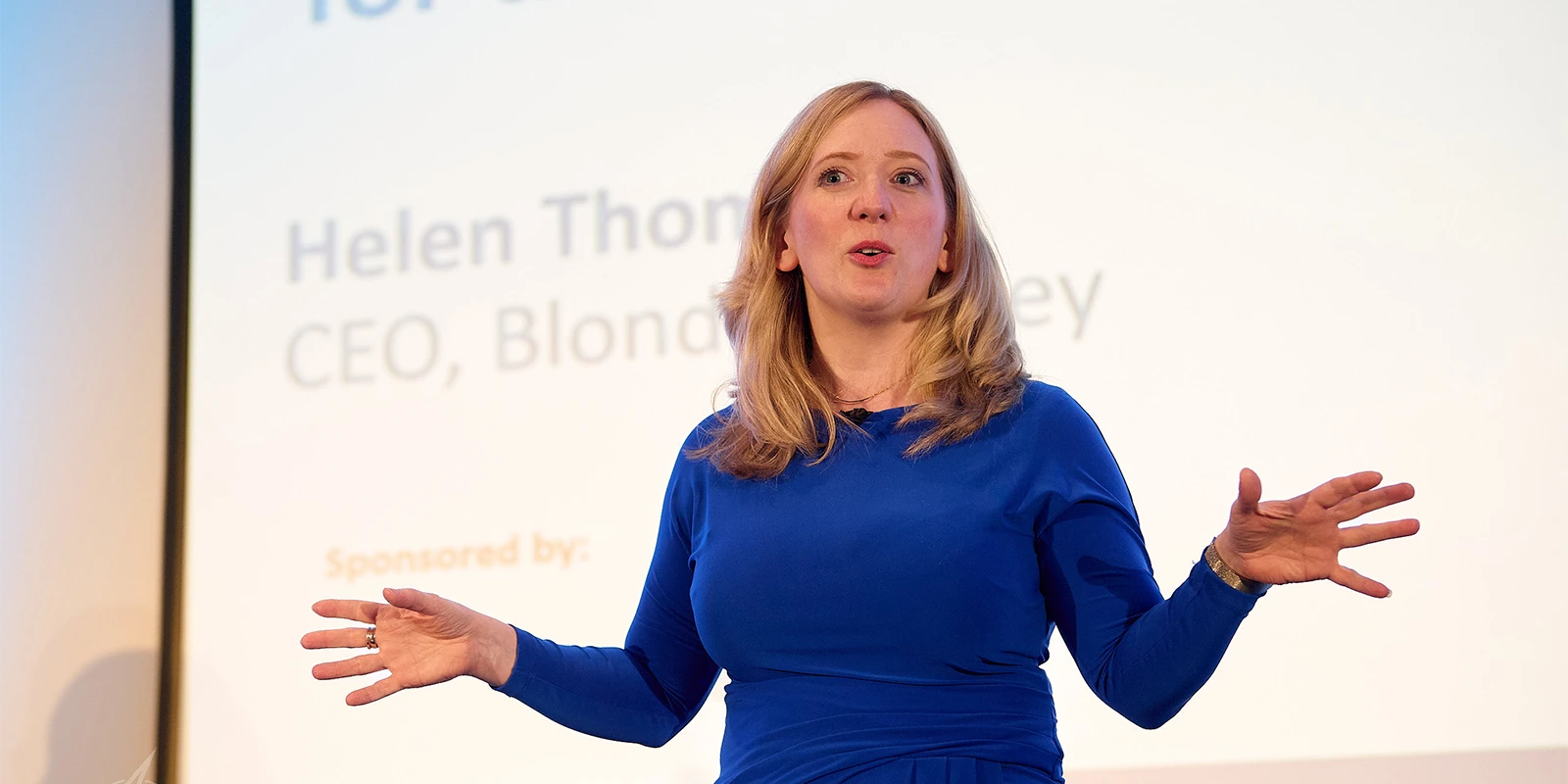 Helen Thomas on stage at a conference, mid-gesture, fully engaged with her audience