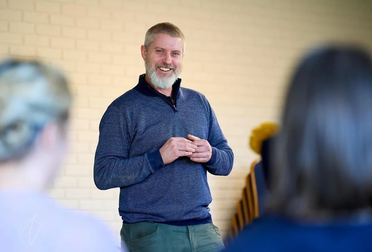 Male speaker in a relaxed setting, smiling naturally while addressing a small group without a lectern or event branding