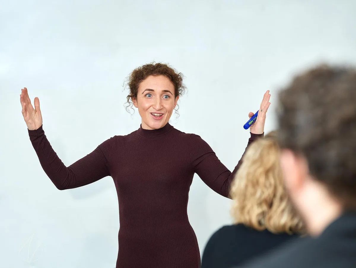 Female presenter with both arms raised wide, fully engaged and expressive during a workshop session