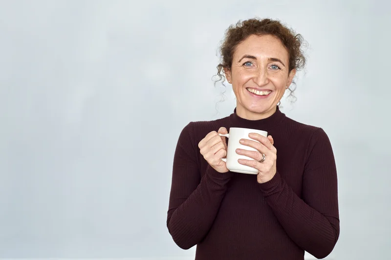 Lizzie Butler standing against a clean background, holding a mug and smiling warmly