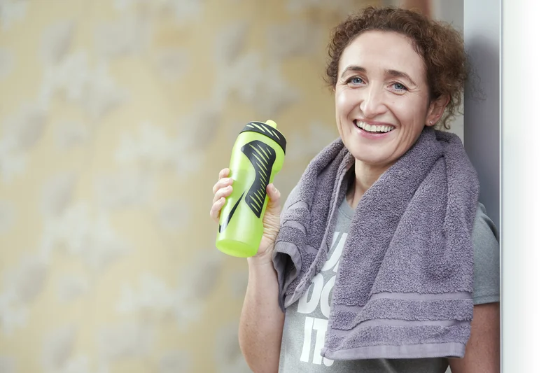 Lizzie Butler post-workout, smiling broadly with a towel around her neck and a water bottle in hand
