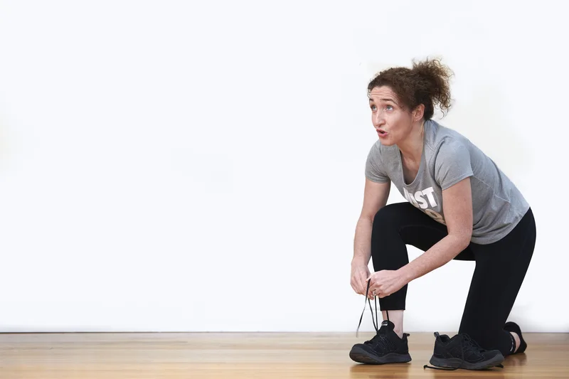 Lizzie Butler crouching to tie her running shoes, caught mid-movement with a playful expression