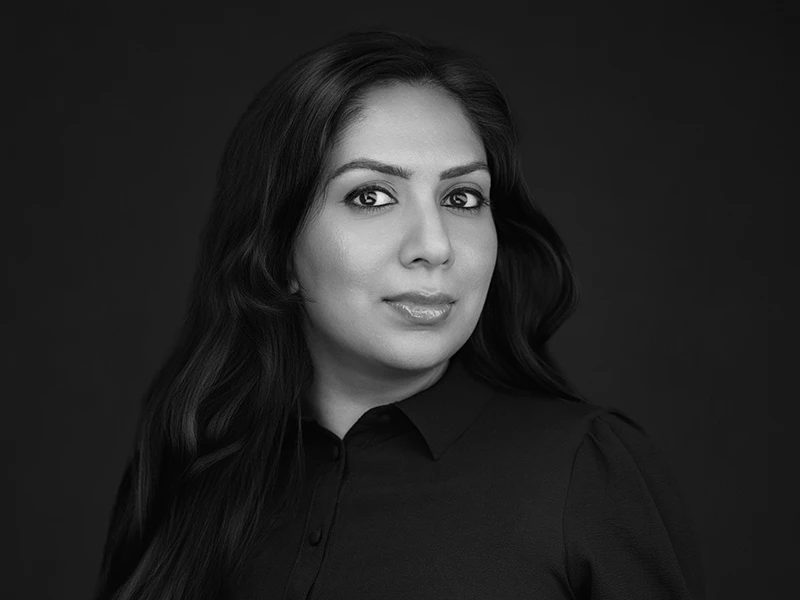Black and white corporate headshot of a woman with long dark hair against a dark background.