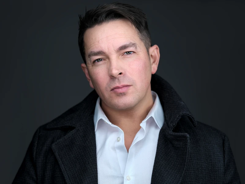 Corporate headshot of a man in a dark coat and white shirt against a dark background.
