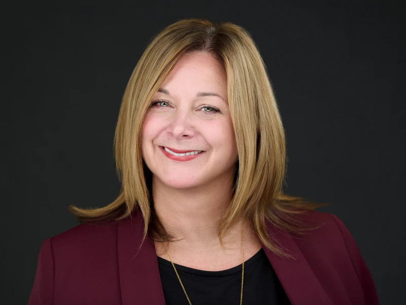 Corporate headshot of a woman in a burgundy blazer on a dark background