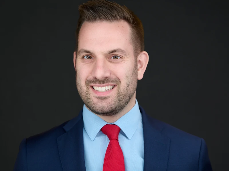 Corporate portrait of a man in a suit and red tie on a dark background