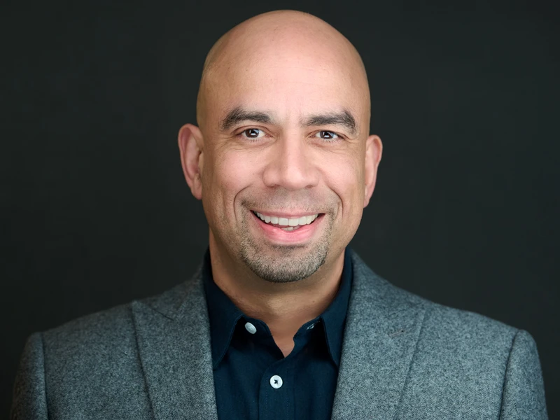 Corporate portrait of a man in a grey blazer on a dark background