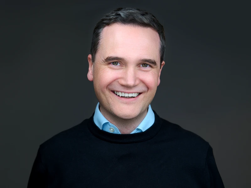 Modern corporate headshot of a man in a black jumper on a dark background