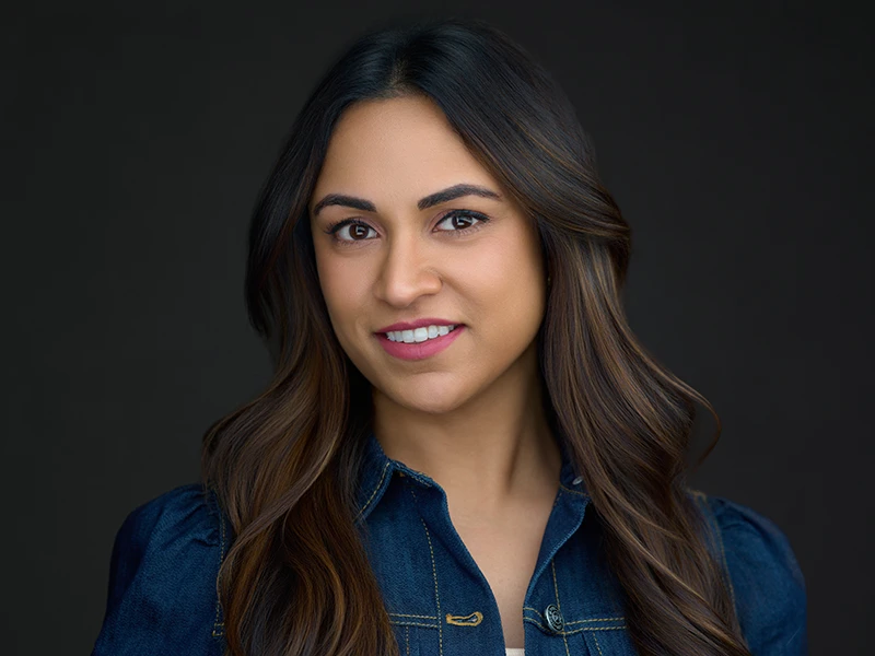 Corporate headshot of a woman in a denim jacket against a dark background, smiling.