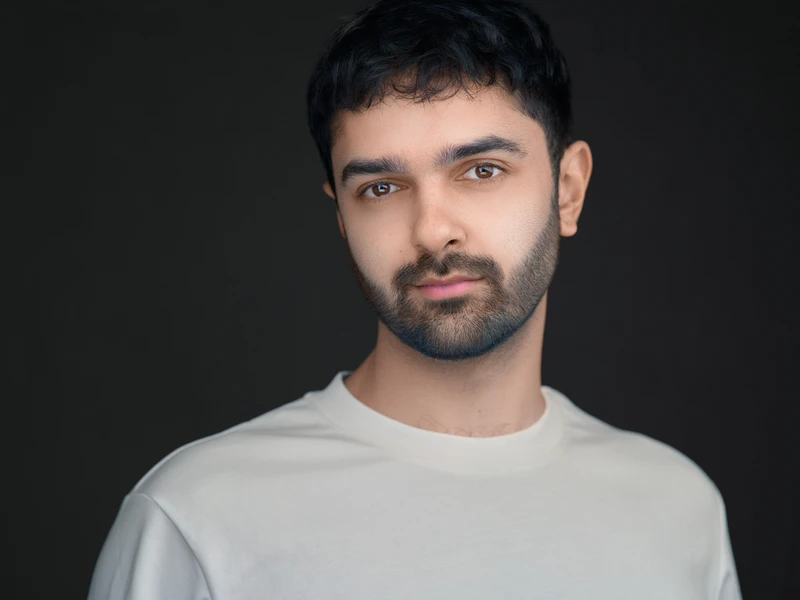 Corporate headshot of a man in a light top against a dark background.