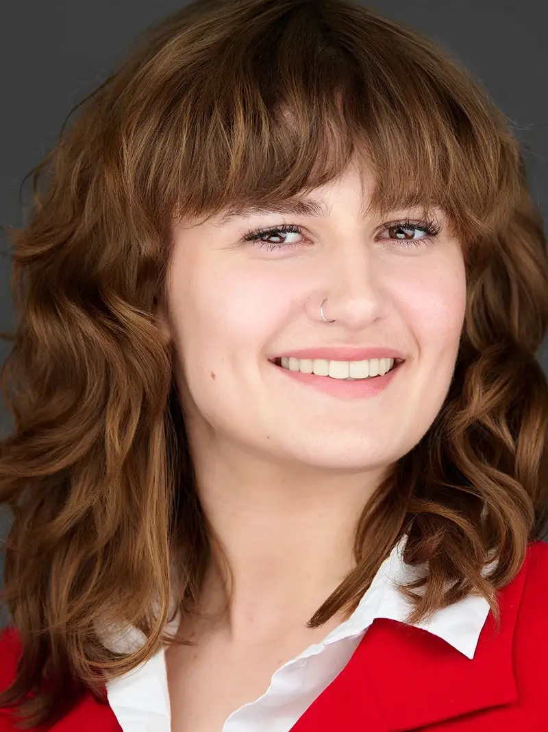 Professional headshot of a smiling woman in a red blazer on a dark background with ample space for headline text.