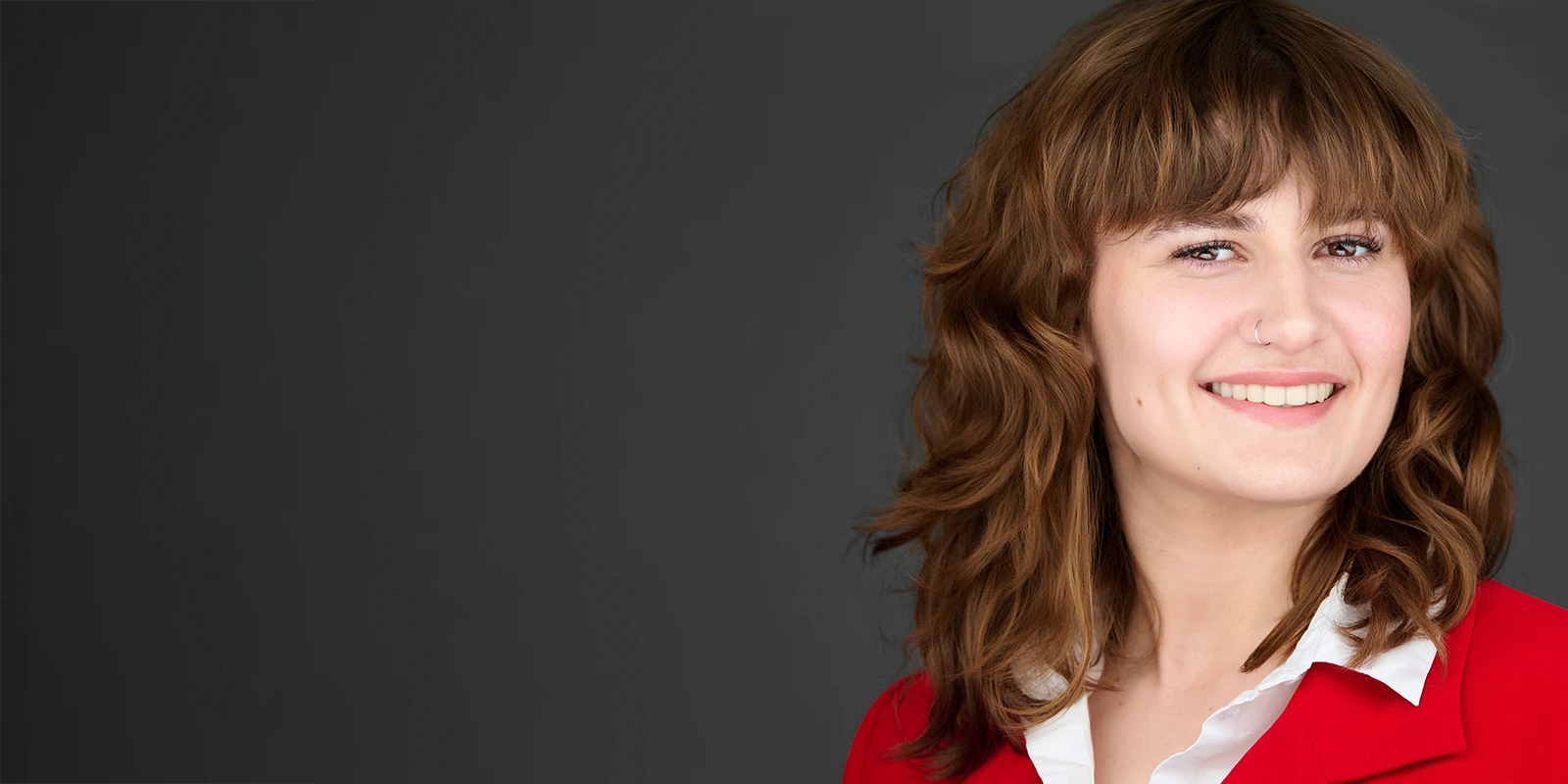 Professional headshot of a smiling woman in a red blazer on a dark background with ample space for headline text.
