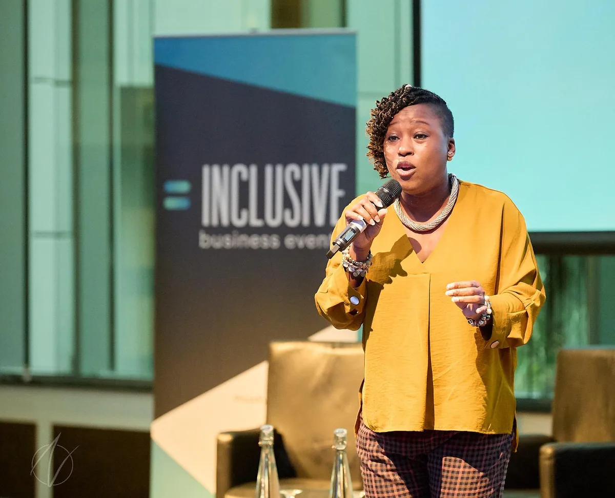 Female speaker holding a handheld microphone on stage, demonstrating confident delivery at a business conference