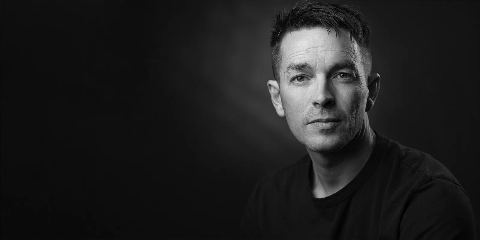 Black and white close-up of Davey Jones in a dark t-shirt, calm and direct expression on a moody studio background