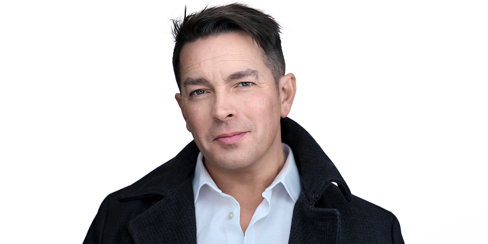 Davey Jones actor headshot on a white background, dark coat and open-collar shirt