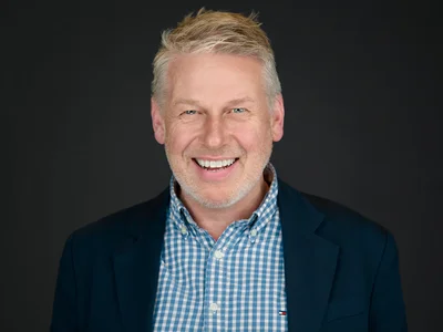 A bearded man in an open-collar blazer, natural expression with clean studio lighting