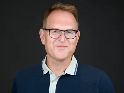 A man in a polo shirt and glasses, relaxed and approachable studio portrait