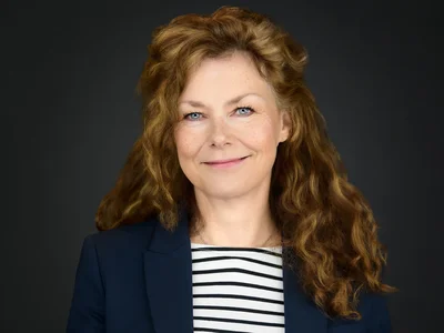 A woman in a smart dark blazer, direct gaze and confident expression