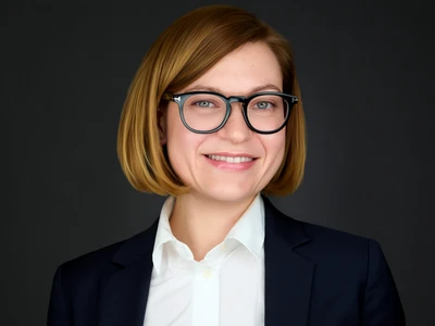 A woman in a blazer, dress shirt and glasses, poised and focused expression