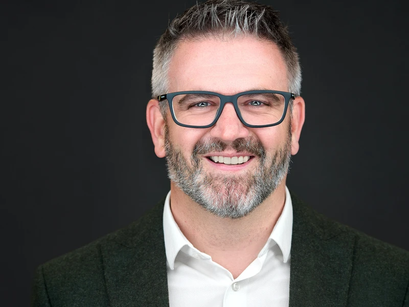 Bearded man in glasses and a blazer, London professional headshot on a dark studio background