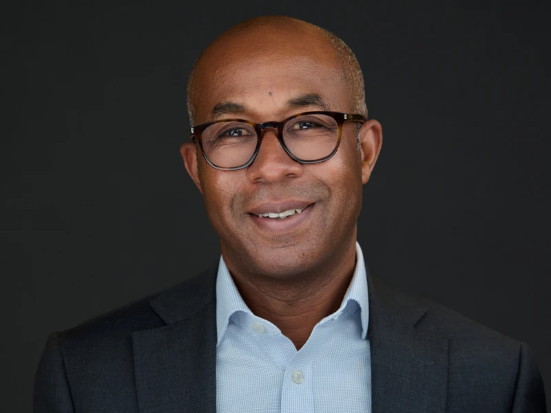 Man in blazer and glasses with open collar, thoughtful and composed headshot