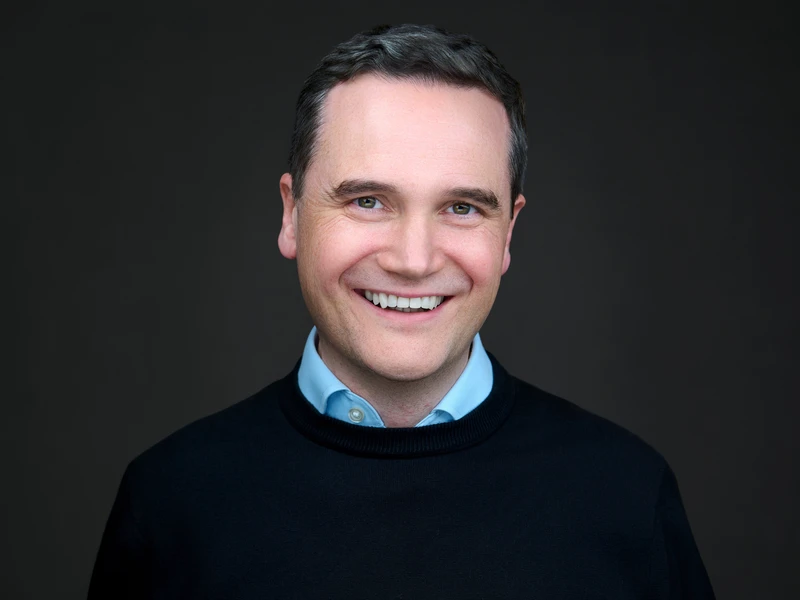 Professional man in a charcoal jumper, relaxed and approachable expression against a dark studio background