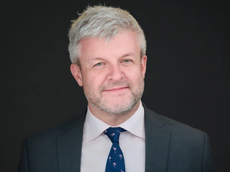 Bearded man in dark suit, authoritative and direct expression, corporate headshot
