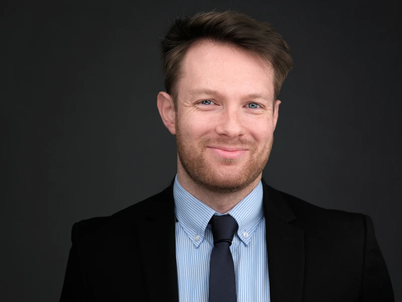 Professional headshot of a bearded man in a dark suit, composed natural expression