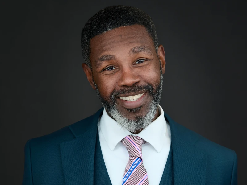 Bearded man in a dark suit, polished executive headshot against a charcoal studio background