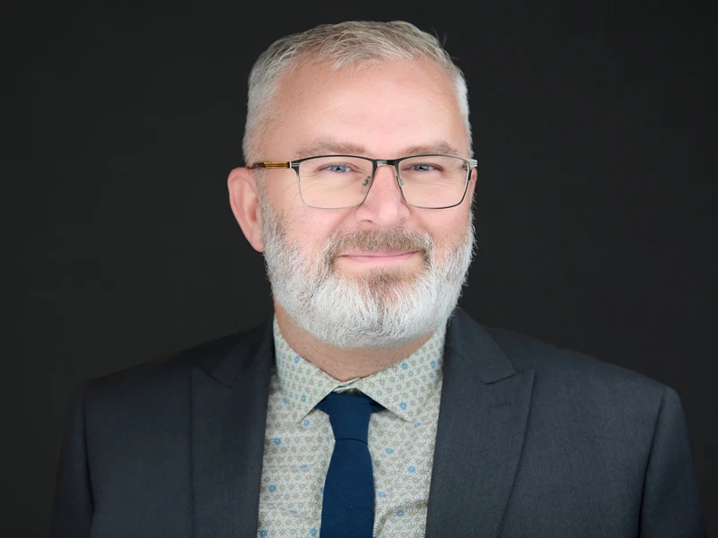 Bearded man in a suit and glasses, professional headshot with quiet authority