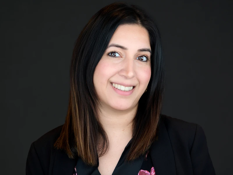 Woman in a smart dark blazer, natural relaxed smile, professional headshot on a dark background