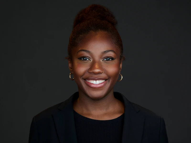 Professional woman in a blazer, composed and engaged, corporate portrait on a dark grey background